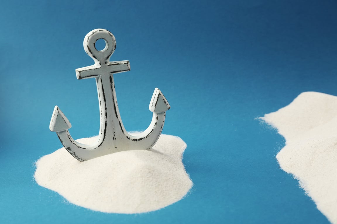 Old Anchor in Sand on Blue Background